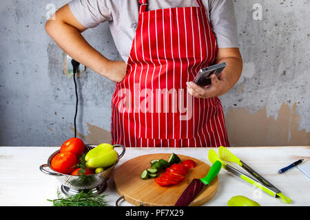 Frau in einem roten Schürze mit Telefon in der Küche. Stockfoto