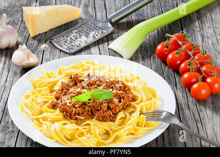 Bolognese Ragout mit italienischer Pasta auf einer weißen Platte, dekoriert mit Basilikumblätter, authentische Rezept, Holz- Hintergrund mit Sellerie, Knoblauch, Cherry tom Stockfoto