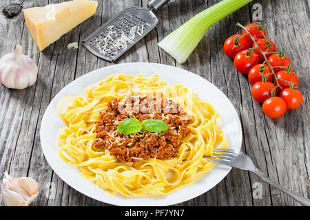 Bolognese Ragout mit italienischer Pasta auf einer weißen Platte, dekoriert mit Basilikumblätter, authentische Rezept, Holz- Hintergrund mit Sellerie, Knoblauch, Cherry tom Stockfoto