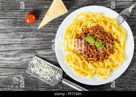 Bolognese Ragout mit italienischer Pasta auf einer weißen Platte, dekoriert mit Basilikumblätter, authentische Rezept, Holz- Hintergrund mit Sellerie, Knoblauch, Cherry tom Stockfoto