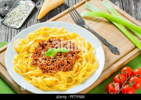 Bolognese Ragout mit italienischer Pasta auf einer weißen Platte, dekoriert mit Basilikumblätter, authentische Rezept, Holz- Hintergrund mit Sellerie, Knoblauch, Cherry tom Stockfoto