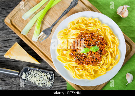 Bolognese Ragout mit italienischer Pasta auf einer weißen Platte, dekoriert mit Basilikumblätter, authentische Rezept, Holz- Hintergrund mit Sellerie, Knoblauch, Cherry tom Stockfoto