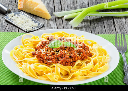 Bolognese Ragout mit italienischer Pasta auf einer weißen Platte, dekoriert mit Basilikumblätter, authentische Rezept, Holz- Hintergrund mit Sellerie, Knoblauch, Cherry tom Stockfoto