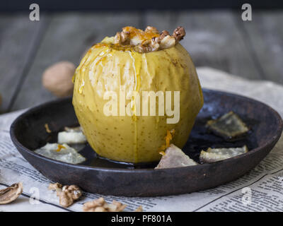 Gelbe Bratapfel mit Zimt, Melone, Nüssen und Honig auf einem schwarzen gusseisernen Schüssel auf einem hölzernen Hintergrund. Herbst oder Winter Dessert. Gesund Stockfoto