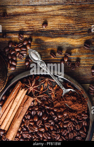 Kaffee Bohnen mit Spooonful gemahlenen Kaffee, Zimtstangen, Sternanis an der Platte. Einige Bohnen verstreut auf Holztisch. Blick von oben. Vertikale Stockfoto