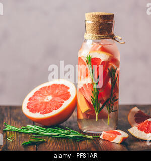 Flasche Detox Wasser hineingegossen mit in Scheiben geschnittenen Rohen Grapefruit und frischen Quellen von Rosmarin. Und Zutaten auf hölzernen Tisch. Stockfoto
