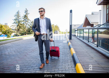 Geschäftsmann zu Fuß von Hotel Lobby. In voller Länge Porträt der jungen Executive mit einem Koffer. Stockfoto