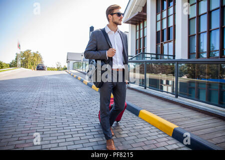 Geschäftsmann zu Fuß von Hotel Lobby. In voller Länge Porträt der jungen Executive mit einem Koffer. Stockfoto