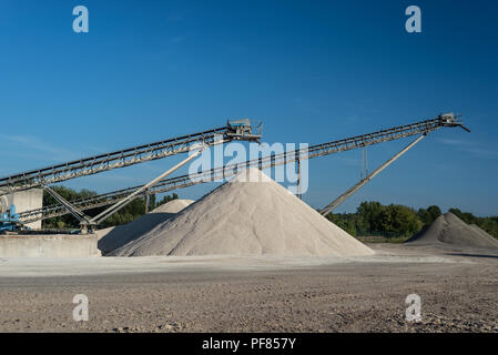 Förderband über Haufen von Kies auf blauen Himmel bei einem industriellen Zementwerk. Stockfoto