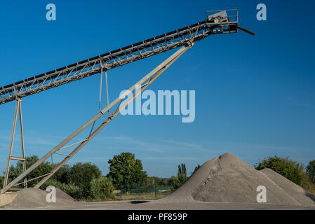 Förderband über Haufen von Kies auf blauen Himmel bei einem industriellen Zementwerk. Stockfoto