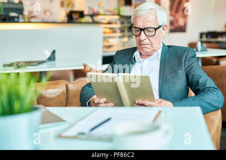 Älterer Mann Lesung buchen Sie im Cafe Stockfoto