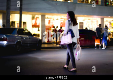 Verschwommenes Konzept Frau über die Strasse mit Einkaufstasche in der Nacht Stockfoto