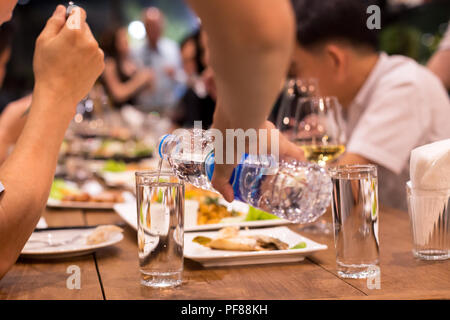 Candin Wwaiter gießt Wasser aus der Flasche, während die Leute in dinne im Restaurant Schuß in hohe ISO bei schwachem Licht Stockfoto