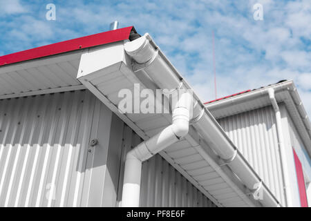 Weiß Regenrinne auf einem Haus mit rotem Dach gegen den blauen Himmel. Kunststoff Dachrinnen System. Regenrinne Abfluss Rohr außen Stockfoto