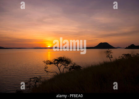 Ein Blick auf den Sonnenuntergang über der Insel Komodo am Horizont, mit Blick auf das Meer und die Inseln in den Vordergrund, wie aus einem Vorgewende auf Flores, Komodo, Indonesien Stockfoto