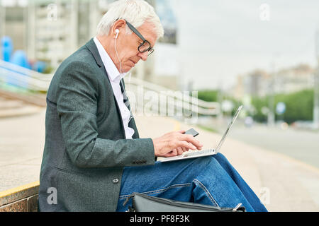Alter Geschäftsmann mit Laptop und Anhören von Musik Stockfoto