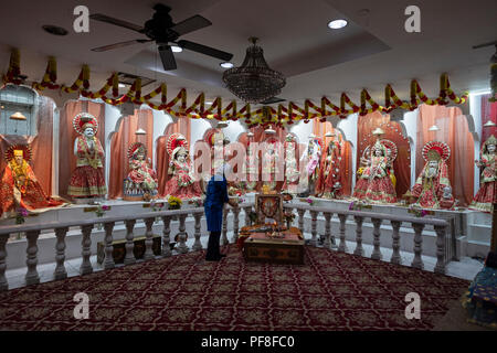 Ein Hindu Frau betet und meditiert vor Statuen von Gottheiten an der Satya Narayan Mandir in Elmhurst, Queens, New York. Stockfoto