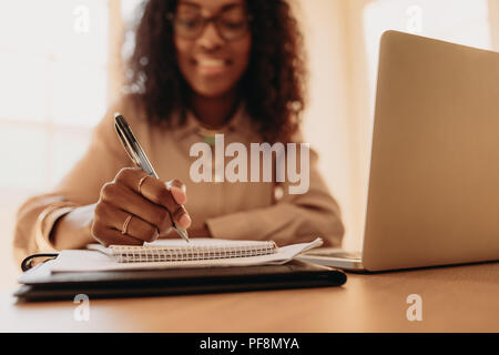 Geschäftsfrau am Laptop zu Hause sitzen. Nahaufnahme der Hand einer Frau mit Stift und schreiben auf Notepad. Stockfoto