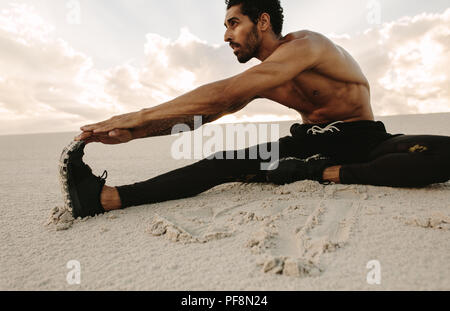 Athleten zu tun stretching Training sitzen auf Sand dune. Runner sitzt in der Wüste und Strecken die Beine. Stockfoto