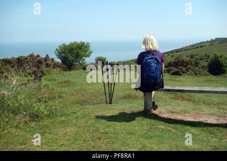 Blonde Frau sitzt auf der Bank aus Holz mit vier Stöcke auf der South West Coastal Path, Somerset, England, UK. Stockfoto