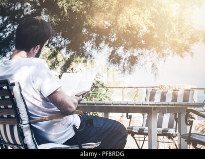 Mann sitzt im Garten Tisch ein Buch lesen Stockfoto