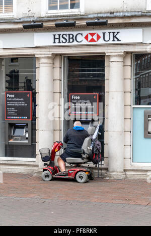 Mann auf Mobilität scooter mit einem ATM Geldautomaten außerhalb einer britischen Bank Stockfoto