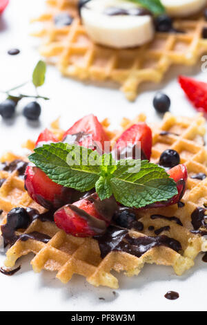 Waffeln mit frischen Beeren - Erdbeere, Heidelbeere, Bananen und Schokolade Topping. Süße Nachspeise auf weißem Hintergrund. Close Up. Stockfoto