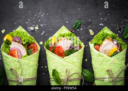 Trendy essen. Grüne Spinat Tortilla mit Hähnchen und Gemüse. Draufsicht auf Schwarz. Gesunden Snack. Stockfoto