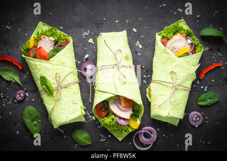 Trendy essen. Grüne Spinat Tortilla mit Hähnchen und Gemüse. Draufsicht auf Schwarz. Gesunden Snack. Stockfoto