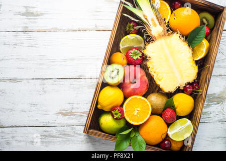 Obst und Beeren im Holzkasten über weiße Holztisch. Ansicht von oben mit der Kopie. Ananas, Zitrusfrüchte und Berry mix. Stockfoto