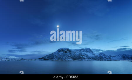 Schneebedeckte Berge gegen den blauen Himmel mit Wolken und Mond im Winter in der Nacht auf den Lofoten Inseln, Norwegen. Arktische Landschaft mit Blick auf das Meer, die verschneite Felsen, mo Stockfoto