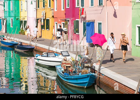 Canal Szene im Abendlicht, Insel Burano, Venedig, Venetien, Italien mit bunten Häusern, einem alten Fischerboot, Reflexionen und Menschen Stockfoto