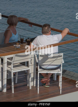 Ein Mann und eine Frau Paar in einem Restaurant sitzen, die Sonne über dem Meer in Kerkyra, Korfu, Griechenland. Stockfoto