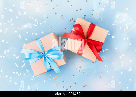 Zwei Geschenkboxen in braunes Packpapier eingewickelt und mit Band auf blauem Hintergrund mit Konfetti dekoriert gebunden. Ansicht von oben, Geschenkidee für Sie und Ihn. Stockfoto