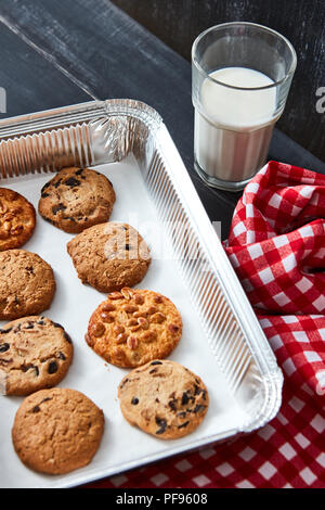 Backblech mit hausgemachten Keksen für Santa mit Erdnüssen, Chocolate Chips, Rosinen und ein Glas mit Milch auf einem dunklen Hintergrund mit einem Handtuch. Stockfoto