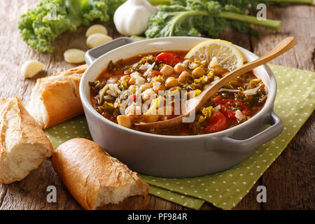 Gesundes Essen: eine dicke Suppe mit Kichererbsen, Grünkohl, Tomaten, Knoblauch und Kartoffeln mit Zitrone schließen in einer Schüssel auf dem Tisch. Horizontale Stockfoto