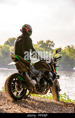 Mann mit Motorradhelm und Sicherheit einheitliche sitzen auf dem Fahrrad im Freien, schönen Landschaft auf dem Hintergrund in Tag einstellen. Stockfoto