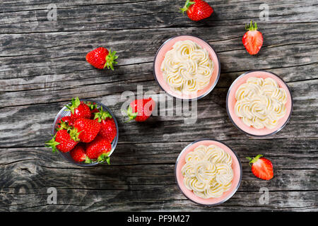 Erstaunlich Strawberry Cheesecake Mousse Cups durch hausgemachtes Eis auf einem alten rustikalen Holztisch eingerichtet, Studio leuchten, Ansicht von oben Stockfoto