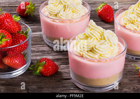 Erstaunlich Strawberry Cheesecake Mousse Cups durch hausgemachtes Eis und ein Glas mit frischen Erdbeeren auf einem alten rustikalen Holztisch eingerichtet, Studio ligh Stockfoto