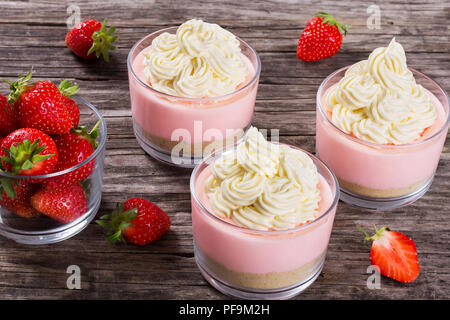 Erstaunlich Strawberry Cheesecake Mousse Cups durch hausgemachtes Eis auf einem alten rustikalen Holztisch eingerichtet, Studio leuchten, Ansicht von oben Stockfoto
