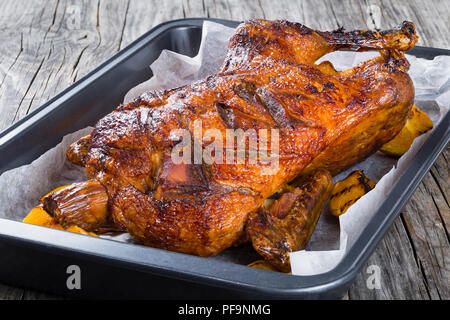 Gebratene ganze Ente in Honig Senf Soja Glasur in eine gebackene Teller mit gegrillten Orangenscheiben auf einem alten rustikalen Tisch, close-up Stockfoto