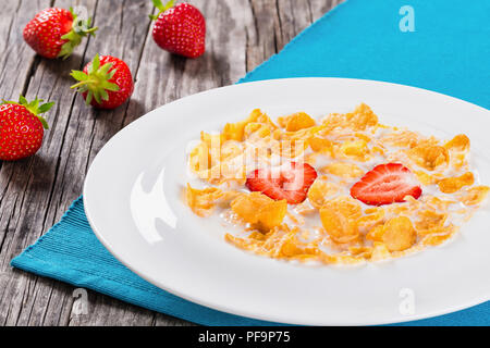 Gesunde Cornflakes mit Milch und Erdbeeren in einen weissen Teller auf einem alten rustikalen Tisch, Studio leuchten, Nahaufnahme, Ansicht von oben Stockfoto