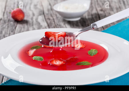 Gekühlt Erdbeeresuppe mit Stücken von Erdbeeren und Minze vom Löffel tropft, Studio, Beleuchtung, Blick von oben, in der Nähe Makro Stockfoto