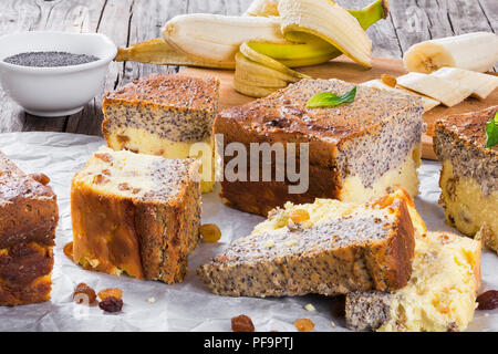 Selbstgemachte Banane Käsekuchen mit Mohn auf einem Pergament Papier auf einem alten Holztisch mit Stücken von Banane und Rosinen, close-up Stockfoto
