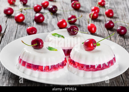 Italienische Dessert von kirschsaft und gesüßte Sahne verdickt mit Gelatine und geformt, auf einem weißen Teller auf einen Tisch Serviette mit Dessert Gabeln und Mellie Stockfoto