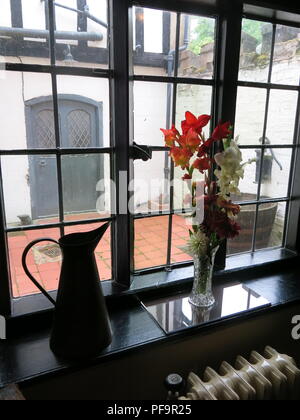Blick aus dem Fenster zum Innenhof an Baddesley Clinton, Warwickshire, Krug & Vase mit Blumen auf der Fensterbank Stockfoto