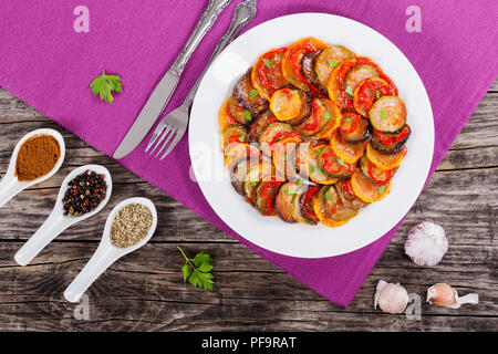 Weiße Platte mit 2-in-1-bunter Gemüseauflauf Ratatouille, Gabel, Messer, Gewürze in Porzellan Löffel auf alte, rustikale Tabelle, Ansicht von Abo Stockfoto