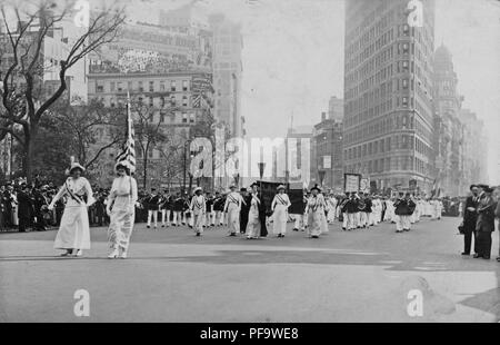 Schwarz-weiß Foto mit mehreren Frauen, tragen weiße Edwardian Kleidung und Schärpen, und Halten einer US-Flagge und Wimpel, gefolgt von einer Blaskapelle, die Teilnahme an einem Wahlrecht Parade in New York City, 1913. () Stockfoto