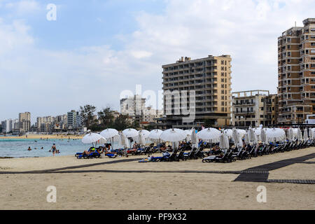 Touristen auf Palm Beach in Famagusta (Gazimagusa) mit verlassenen Hotels und Wohnblocks im Hintergrund, Türkische Republik Nordzypern Stockfoto