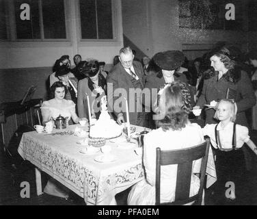 Schwarz-weiß Foto zeigt zwei Frauen, die auf beiden Seiten eine kleine Tabelle, die beladen mit Kerzen, Kuchen und Kaffee, Ausgabe Tassen Tee und Platten Kuchen zu einer Reihe von Menschen, die mit einer kleinen blonden Mädchen im Vordergrund rechts sichtbar, in Ohio, 1955 fotografiert. () Stockfoto